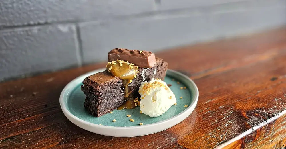 A chocolate brownie with vanilla ice cream and a chocolate caramel slice on a green plate