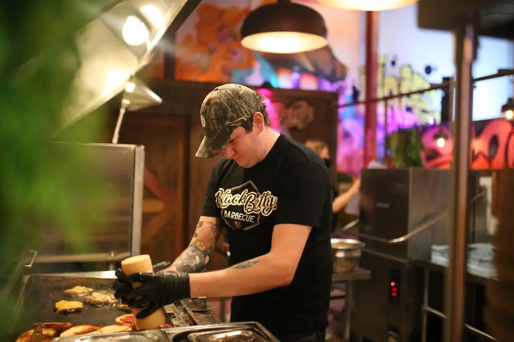 A Black Betty cook laying cheese onto burger patties on the flat top during service