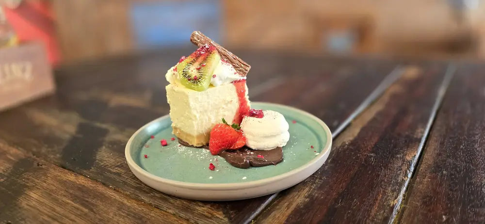 A slice of cheesecake with strawberry, kiwifruit, cream and a chocolate shard