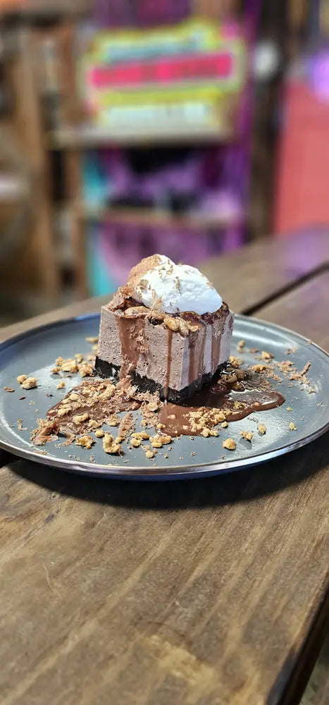 A slice of hokey pokey cheesecake topped with a scoop of vanilla ice cream on a stone plate