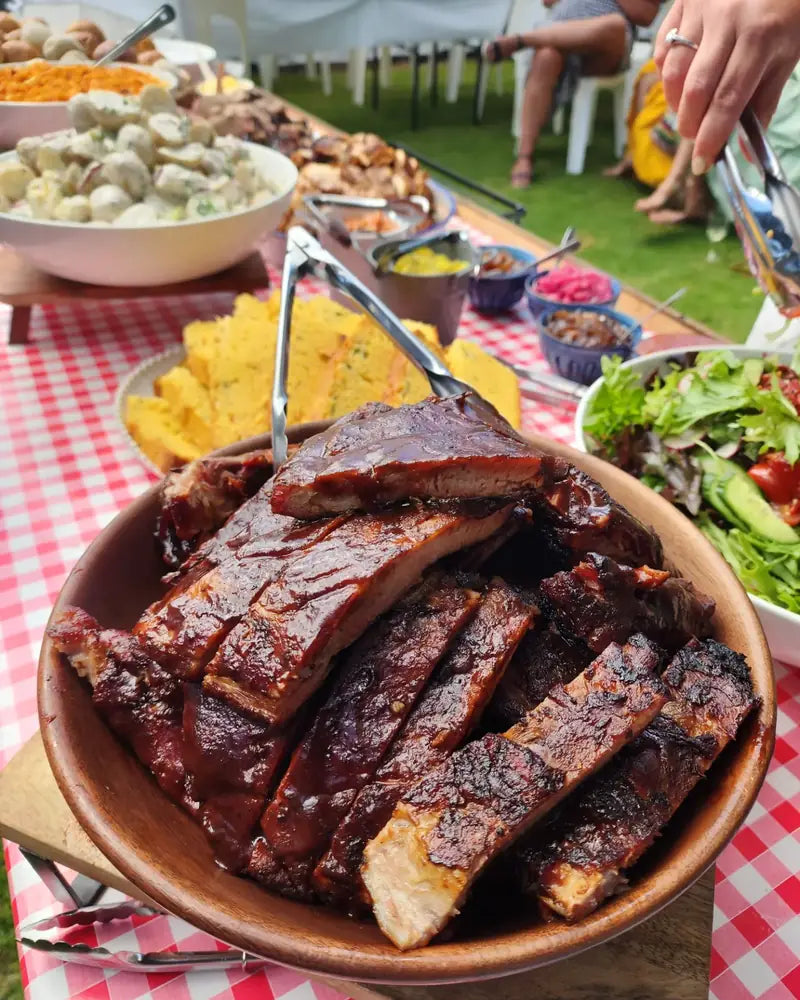 A bowl of glazed ribs in front of a marquee buffet of sides, salads and cornbread