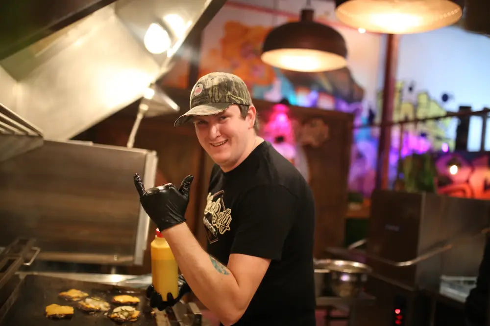 A Black Betty cook in a cap and branded tee working the flat top grill in the Warren Street kitchen