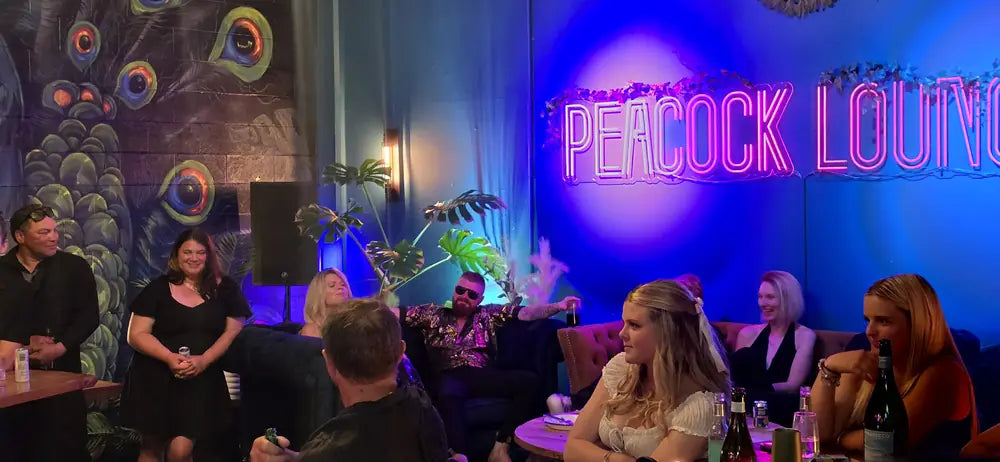 Guests on couches and bar stools with drinks in front of the lit peacock mural
