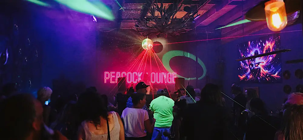 Dancers under a mirror ball and a red laser, the neon Peacock Lounge sign behind them