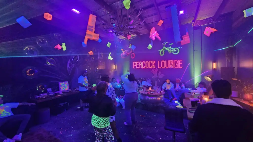 Guests at tables under the neon Peacock Lounge sign, confetti and coloured lights filling the room