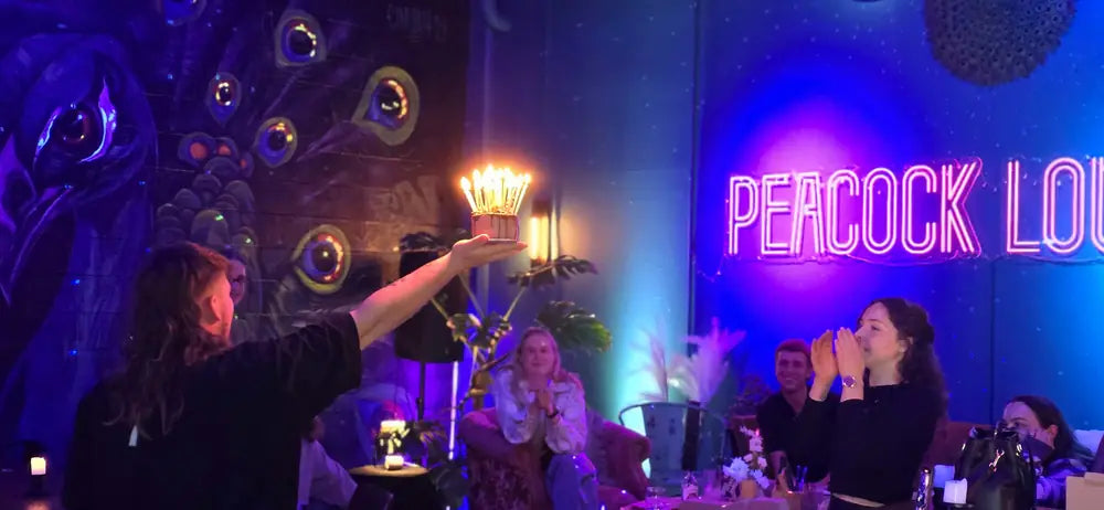 Guests at tables in front of the peacock mural and the pink neon Peacock Lounge sign