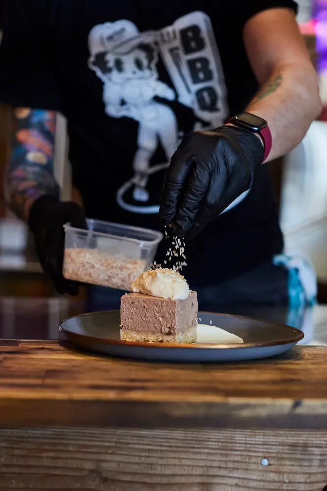 A cook in black gloves dusting a plated dessert during service