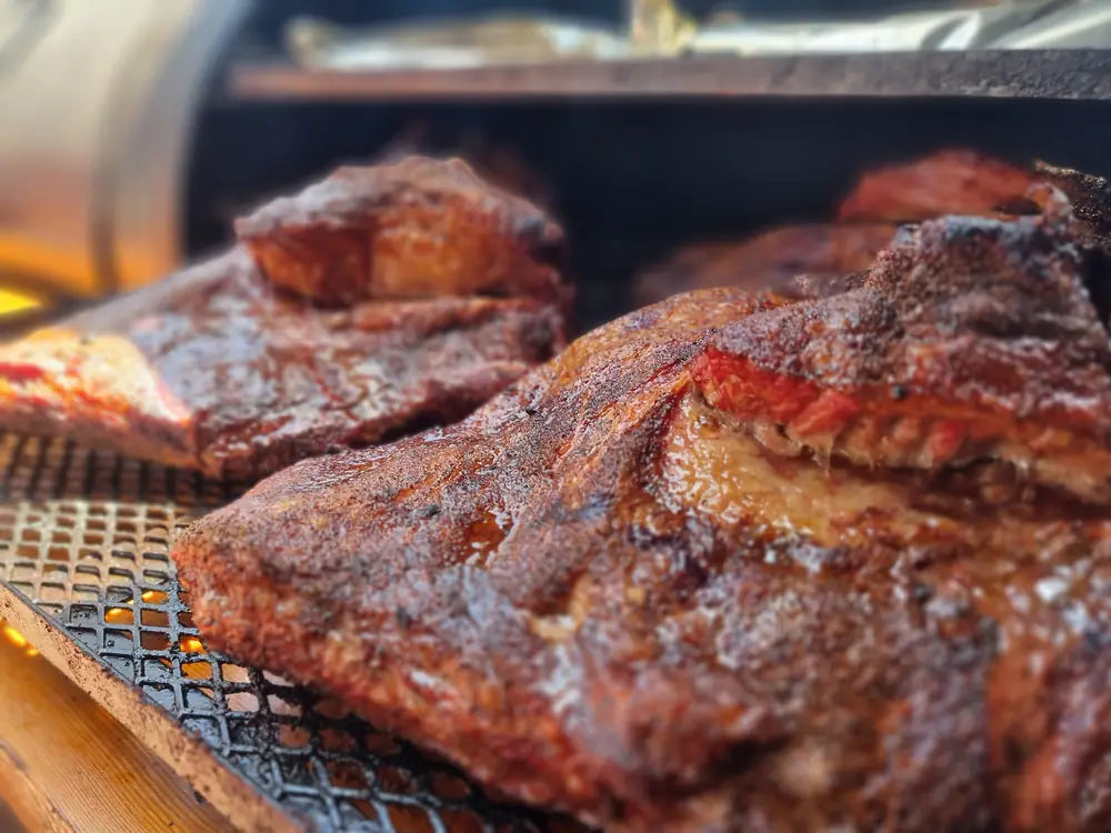 Racks of pork ribs and brisket cooking over coals in the smoker