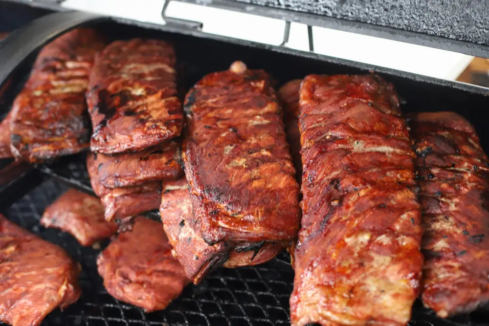 Racks of pork ribs glazed and smoking on the grill bars over hot coals