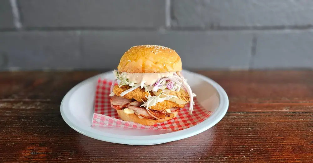 A pulled pork slider with slaw on gingham paper, plated against a grey brick wall