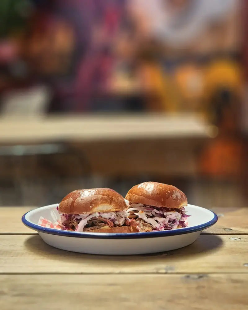 Two pulled pork sliders with slaw in a white enamel bowl on a picnic table