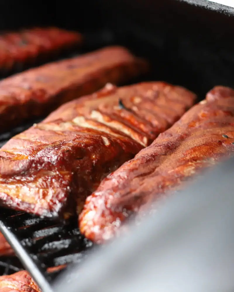 Two racks of glazed pork ribs cooking on the grill bars