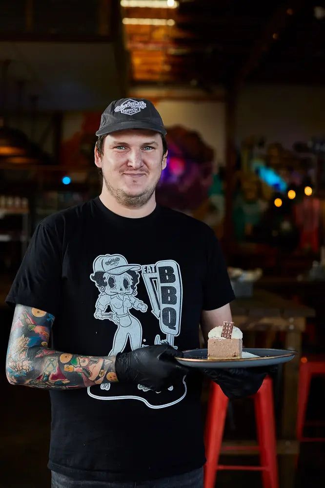 A Black Betty cook carrying a dessert through the restaurant, mural wall and red stools behind