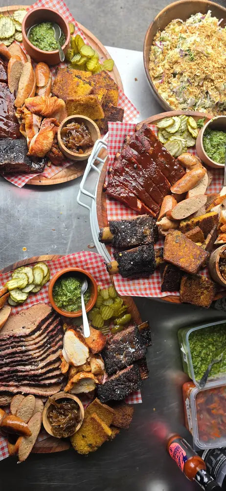 Overhead spread of ribs, brisket, sausage, pickles and sauces on a gingham cloth