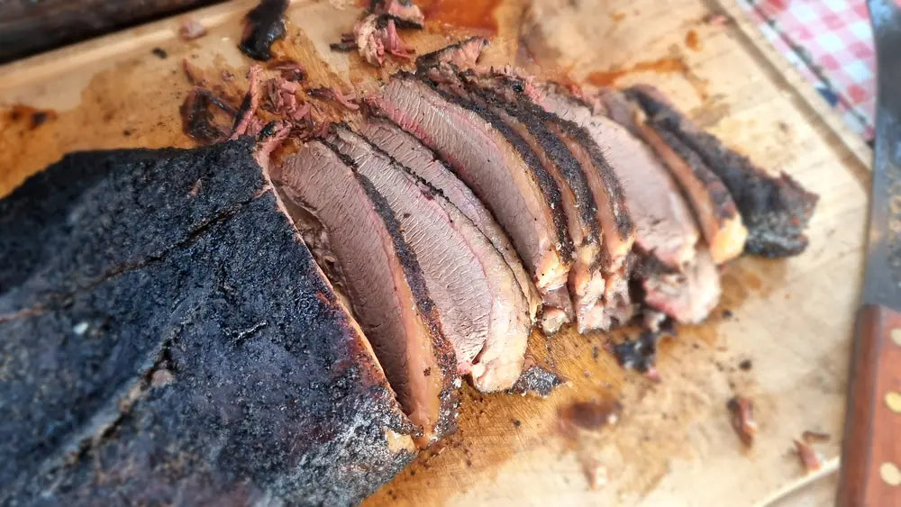 A smoked beef brisket sliced on the board, showing the smoke ring and the bark