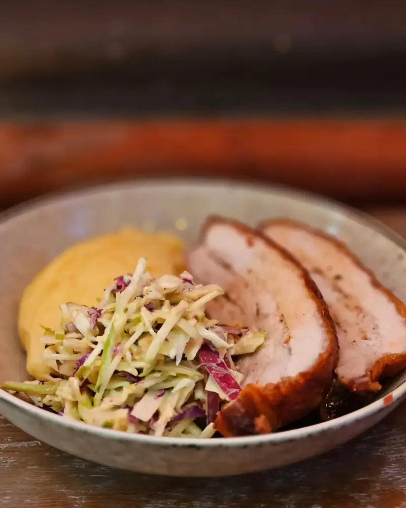 Sliced smoked pork belly with apple slaw and kumara puree in a ceramic bowl