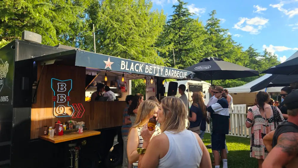Guests with drinks at the Black Betty Barbecue bar trailer during an outdoor event
