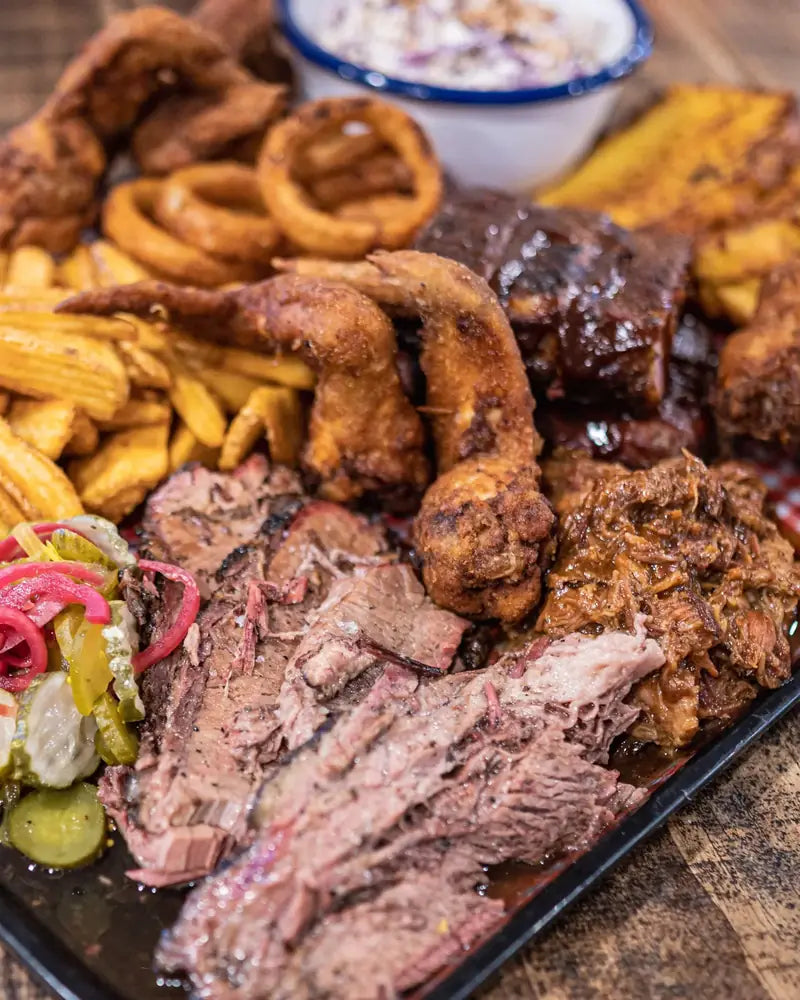 A loaded share board of hot wings, curly fries, ribs, sliced brisket, pulled pork, pickles and slaw