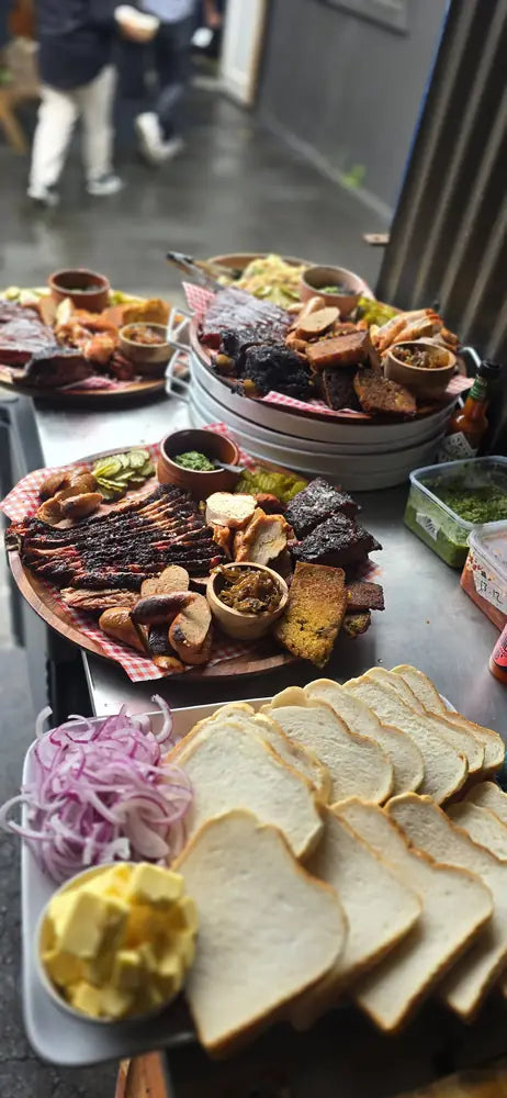 A long table of Black Betty platters, white bread, pickled onion and sides laid out for a group