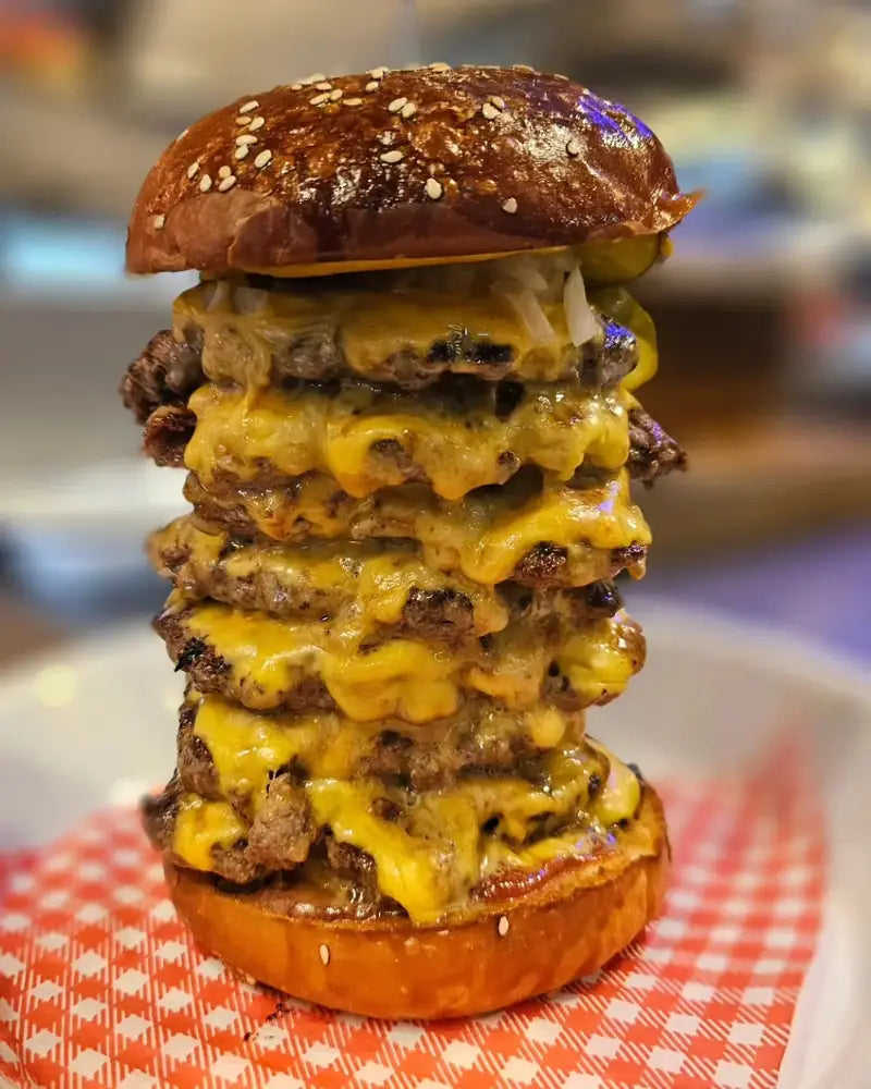 A tower of six smashed beef patties layered with melted cheese in a pretzel bun